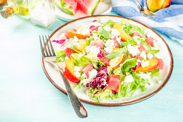 Summer diet salad with leaves of lettuce, watermelon, peach and feta cheese. On a light blue background copy space