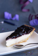 A slice of cheesecake on dark background with lilac serpentine. lifestyle photo of a piece of birthday cake, copy space