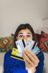 Portrait young woman holding credit cards. Worried face and scared eyes because too much expanses or internet scam during online shopping. Debts, technology, home banking o fraud concept.