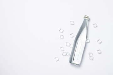 Bottle of pure crystal water with ice cubes on a white background under sunlight. Banner. Concept of thirst, heat, summer, tropic. Flat lay, top view