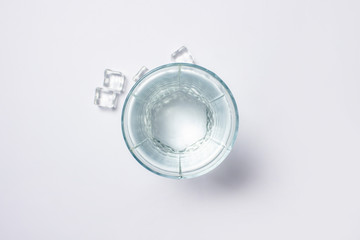 Glass of pure crystal water and ice cubes on a white background under sunlight. Banner. Concept of thirst, heat, summer, tropic. Flat lay, top view