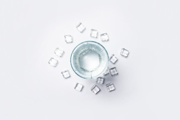 Fototapeta premium Glass of pure crystal water and ice cubes on a white background under sunlight. Banner. Concept of thirst, heat, summer, tropic. Flat lay, top view