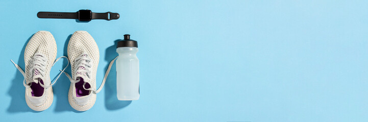 Fitness tracker, White sneakers and a bottle of water under morning sunlight on a blue background.Jogging, running, fitness, cross fit, hard workout. Morning run. Banner. Flat lay, top view