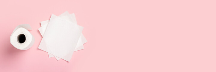 Roll of paper towels and few pieces towels on a pink background. Concept is 100% natural product, delicate and soft. Flat lay, top view. Banner