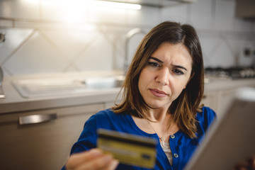 Close up young woman housewife in her kitchen holding tablet for online shopping. Using credit card for internet payment. Home banking, technology concept.