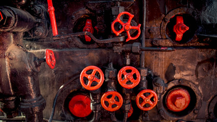 Toned photo of old rusty steam pipes and red valves on steam boiler of old locomotive