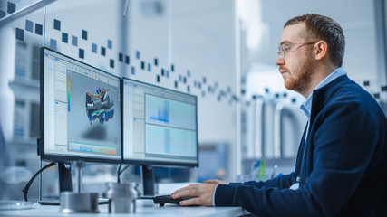 Industrial Engineer Solving Problems, Working on a Personal Computer, Two Monitor Screens Show CAD...