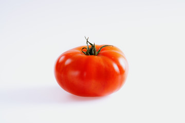 Fresh bright red ripe beefsteak tomato with green stalk on a white background.