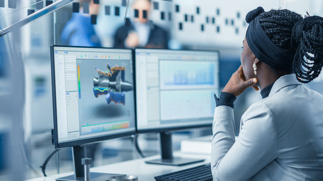 Beautiful Female Engineer Working On Personal Computer In The High-Tech Industrial Factory, She Uses CAD Software Designing 3D Turbine. Over The Shoulder Shot.