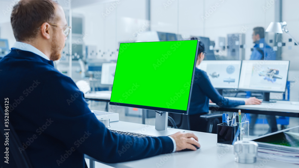 Poster over the shoulder: heavy industry engineer working on personal computer, display is green mock-up sc