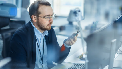 Electronics Factory: Male Electrical Engineer Holds PCB Prototype, Works on Computer, uses CAD...
