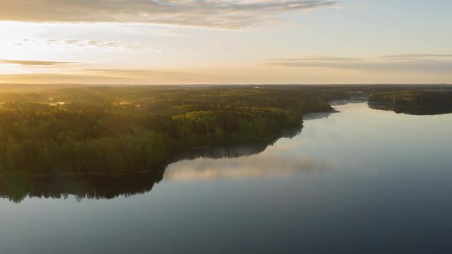 Hyperlapse drone flying over lake at sunrise. Timelapse clouds of fog above water surface. Early morning haze. Haze over river countryside. Pine trees forest on horizon reflected in water