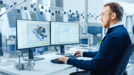 Industrial Engineer Working on a Personal Computer, Two Monitor Screens Show CAD Software with 3D Prototype of Hybrid Electric Engine and Charts. Modern Factory with High-Tech Machinery