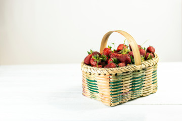 Fototapeta na wymiar Ripe strawberries in little basket on white wooden background. 