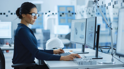 Beautiful Female Engineer Working on Personal Computer in the High-Tech Industrial Factory, She Uses CAD Software to Model Heavy Industry High Tech Mechanism 3D Model. Side View Shot