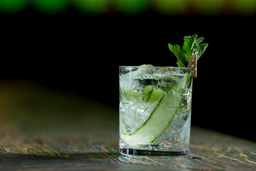 alcoholic cocktail with mint cucumber and liquor in a transparent glass on a dark background with color highlight with bar shots