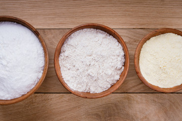 Rice flour, corn flour and whole grain flour in wooden bowls on wooden oak table. Flat lay top view, studio shot
