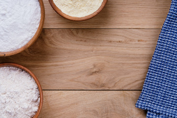 Wooden oak table with rice flour, corn flour and whole grain flour in wooden bowls and blue napkin. Baking ingredients with space for text or image. Flat lay top view, studio shot