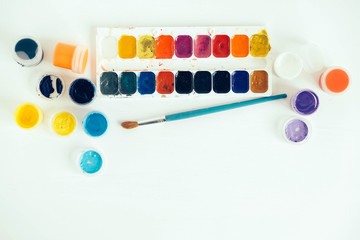 Colorful gouache paints and brush for painting on white wooden table. Top view. Copy, empty space...