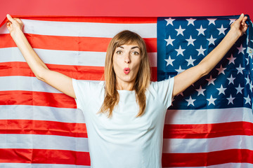 Young girl holds the US flag on a pink background. Concept patriot, holiday, independence day, memorial day, US visa, emigration to USA, education in USA