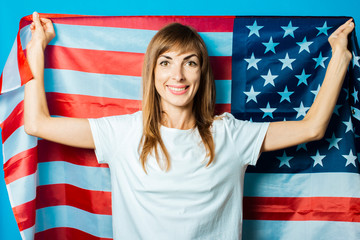 Young woman holds the USA flag on a blue background. USA Visa Concept, English, Independence Day, July 4th, Memorial Day. Travel to the USA