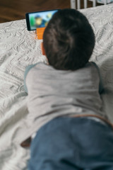 selective focus of little boy watching webinar on smartphone while lying on bed