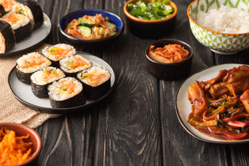 selective focus of traditional gimbap near tasty korean dishes on wooden surface