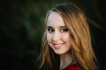 Obraz premium Portrait of a beautiful girl stand in autumn in a red dress against the background of the field on the nature. upper half. look straight ahead. Close up. headshot.