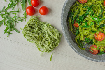 Top view Spinach Tagliatelle pasta with tomatoes and arugula on wooden table with ingredients.