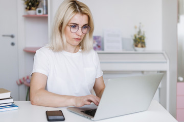 Blonde woman sits at a table and works with a laptop.