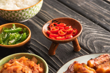 selective focus of green bell peppers near rice, spicy chili peppers and korean side dishes on wooden surface