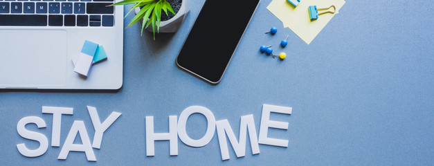 Panoramic crop of gadgets, stationery and plant near stay home lettering on blue surface