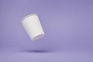 White paper cup of coffee colored background.  Flying paper cup on violet background. Isolated for mock up