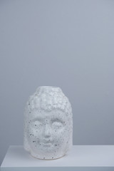 close up white Buddha head on a white table against gray concrete background