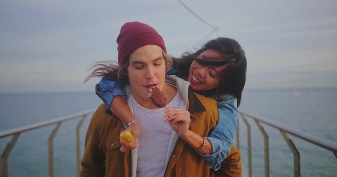 Couple having fun with piggyback ride and ice-cream on pier
