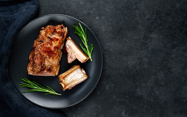 Grilled pork ribs on a black plate with spices on a stone background
with copy space for your text