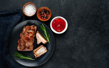 Grilled pork ribs on a black plate with spices on a stone background
with copy space for your text
