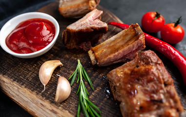 Grilled pork ribs on a cutting board with spices on a stone background