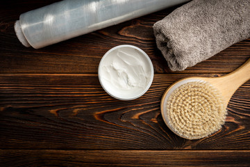 Wooden massage brush, cream and towel on dark wooden background.