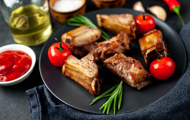 Grilled pork ribs on a black plate with spices on a stone background