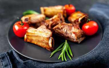 Grilled pork ribs on a black plate with spices on a stone background