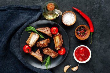 Grilled pork ribs on a black plate with spices on a stone background