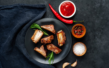 Grilled pork ribs on a black plate with spices on a stone background