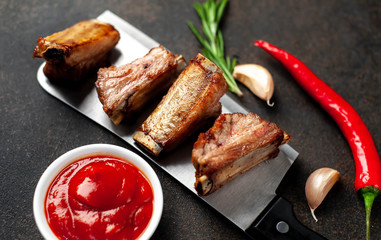 Grilled pork ribs over meat knife with spices on a stone background 