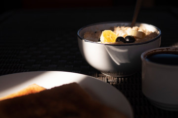 Oatmeal with bananas and berries in the morning light. Coffee, breakfast.