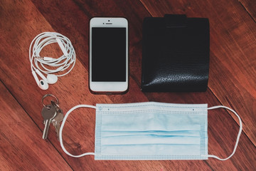 A high angle shot of a smartphone, headphones, wallet, keys and a surgical mask