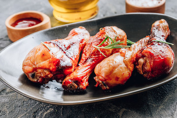 Chicken legs on black plate with red sauce and rosemary on black rustic background.