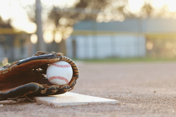Baseball in glove close up with blurred sports field in background at sunset with copy space.