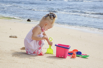 Fototapeta na wymiar Summer vacation. Adorable toddler girl playing with beach toys on the sandy beach.