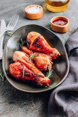 Chicken legs on black plate with red sauce and rosemary on black rustic background.
